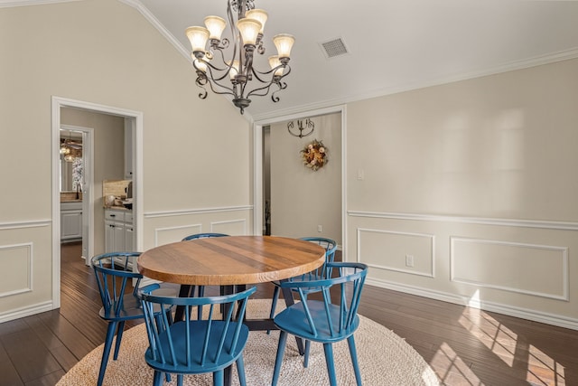 dining space with crown molding, a decorative wall, dark wood finished floors, and a notable chandelier