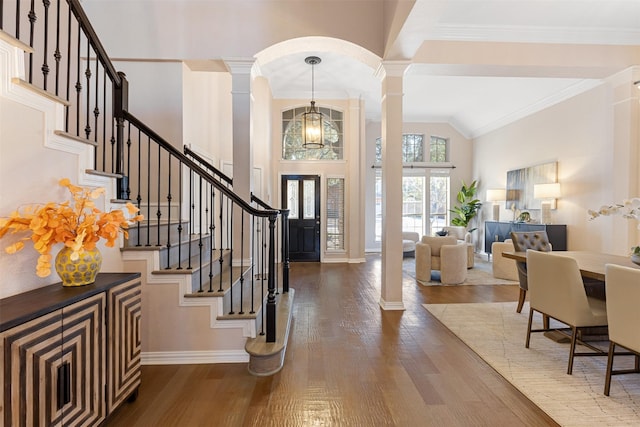 foyer featuring a high ceiling, wood finished floors, crown molding, and ornate columns