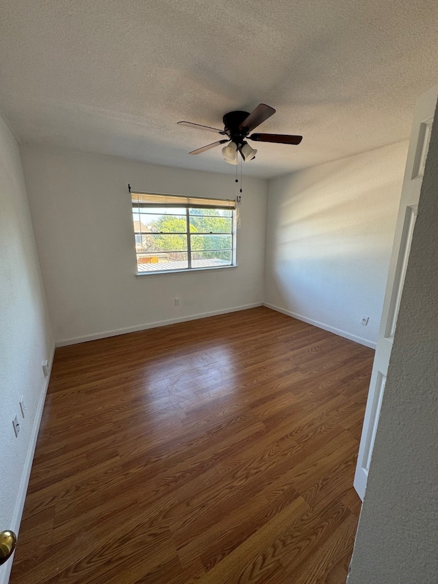 empty room with dark wood-style floors, ceiling fan, a textured ceiling, and baseboards