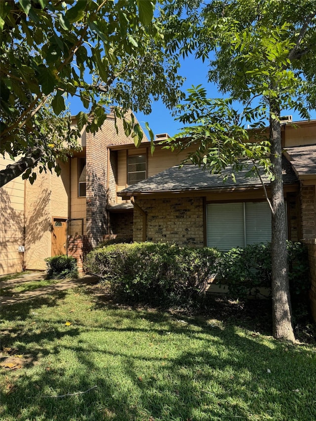 view of side of home with a yard, brick siding, and a shingled roof