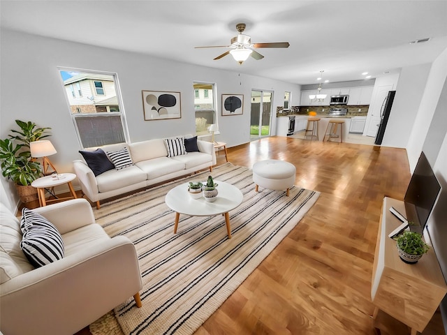 living area featuring visible vents, ceiling fan, light wood-type flooring, and a wealth of natural light