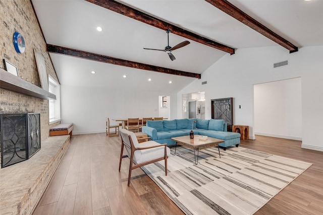 living area with a ceiling fan, a fireplace, light wood-style flooring, and beamed ceiling