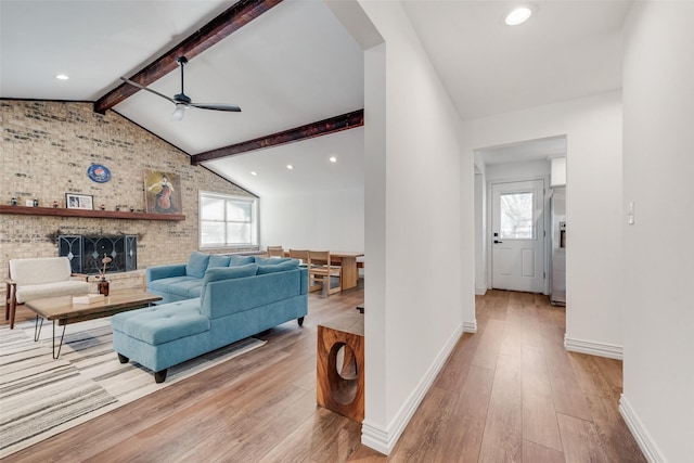 living room featuring light wood finished floors, lofted ceiling with beams, a ceiling fan, a brick fireplace, and baseboards