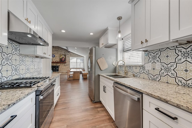 kitchen with white cabinets, appliances with stainless steel finishes, under cabinet range hood, pendant lighting, and a sink