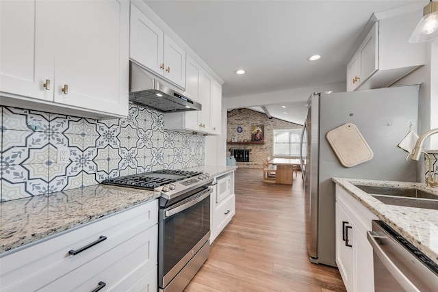 kitchen featuring light stone counters, appliances with stainless steel finishes, white cabinets, vaulted ceiling, and under cabinet range hood