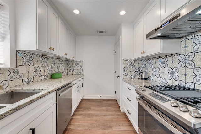 kitchen featuring white cabinets, range hood, light stone counters, and stainless steel appliances