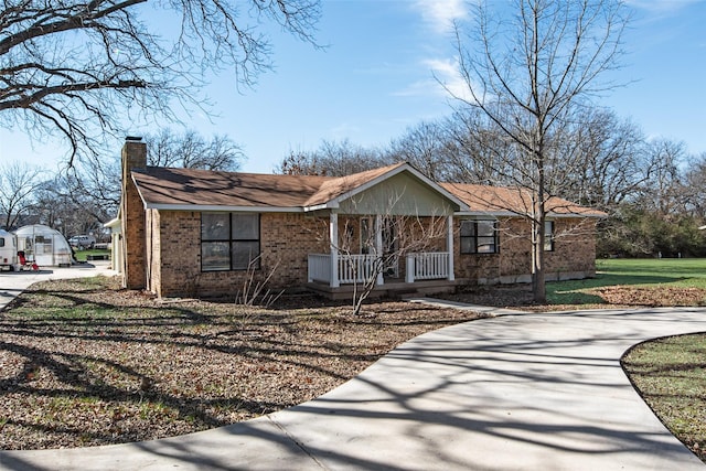 ranch-style house featuring brick siding, a chimney, a porch, concrete driveway, and a front yard