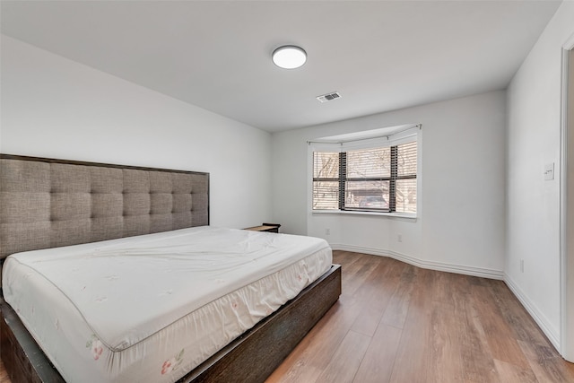 bedroom with baseboards, visible vents, and wood finished floors