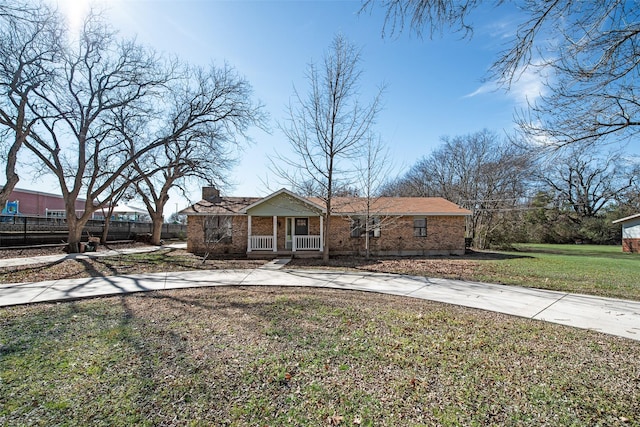 view of front of property featuring concrete driveway, a chimney, a front yard, a porch, and brick siding