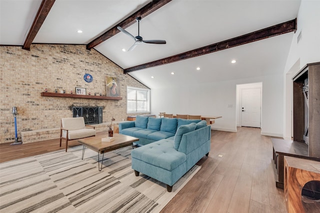 living area with light wood-style flooring, brick wall, ceiling fan, vaulted ceiling with beams, and a brick fireplace