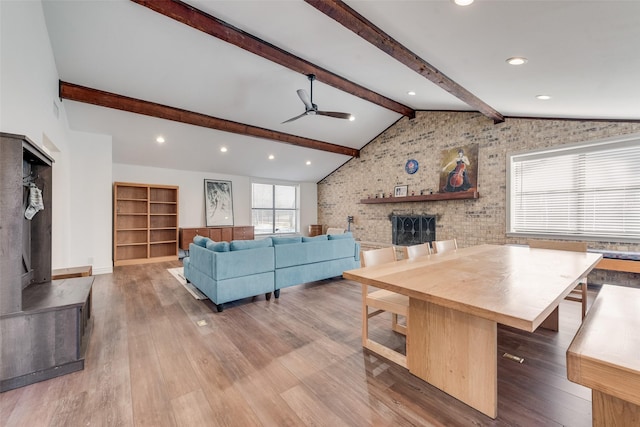 living area featuring vaulted ceiling with beams, recessed lighting, wood finished floors, a ceiling fan, and a brick fireplace