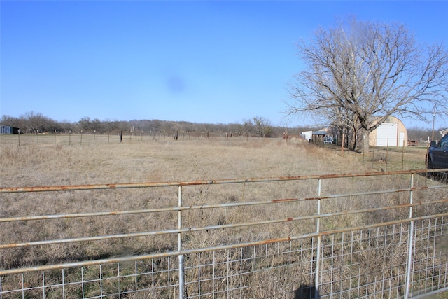 view of yard with a garage, a rural view, and fence