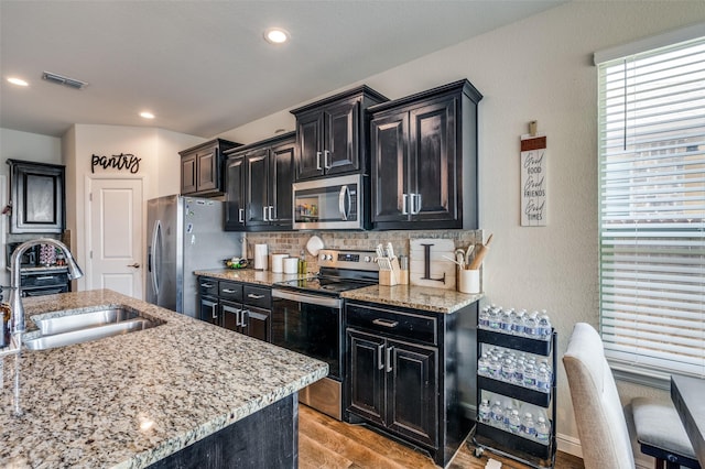 kitchen featuring light stone counters, dark cabinets, a sink, visible vents, and appliances with stainless steel finishes