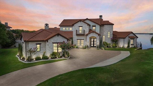 view of front of property with a tile roof, concrete driveway, french doors, a front lawn, and a chimney