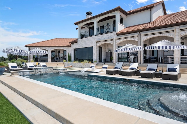 rear view of property with stone siding, a tile roof, a balcony, and a hot tub