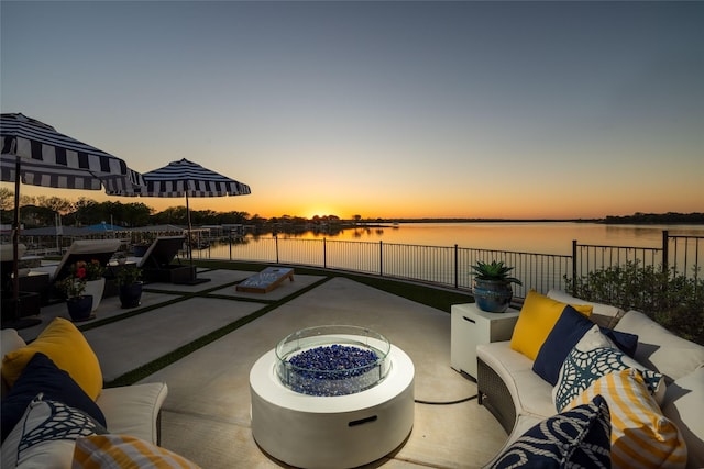 patio terrace at dusk with a water view, fence, and an outdoor living space with a fire pit