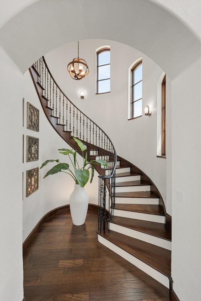 stairs featuring arched walkways, baseboards, wood finished floors, and a chandelier