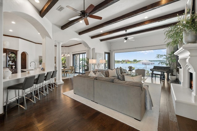 living room with a water view, visible vents, dark wood-type flooring, beamed ceiling, and ornate columns