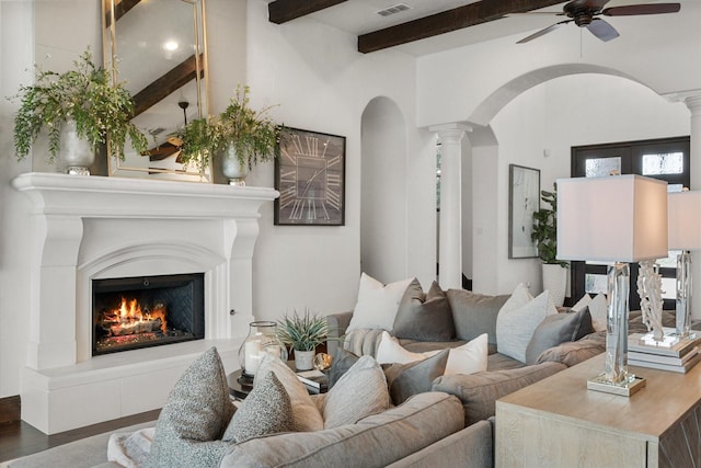 living room featuring a warm lit fireplace, decorative columns, arched walkways, wood finished floors, and beam ceiling