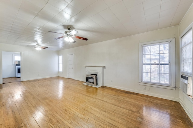 unfurnished living room with light wood-style flooring, a fireplace with flush hearth, a ceiling fan, baseboards, and heating unit