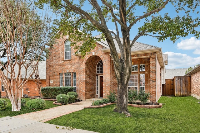 traditional-style home featuring brick siding, fence, driveway, a gate, and a front yard