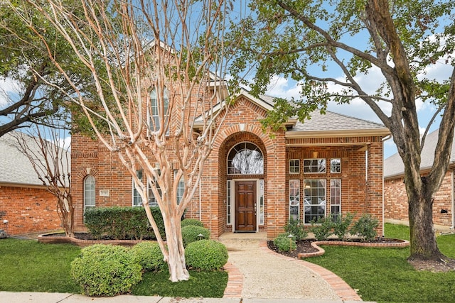 view of front of property featuring a shingled roof, a front yard, and brick siding