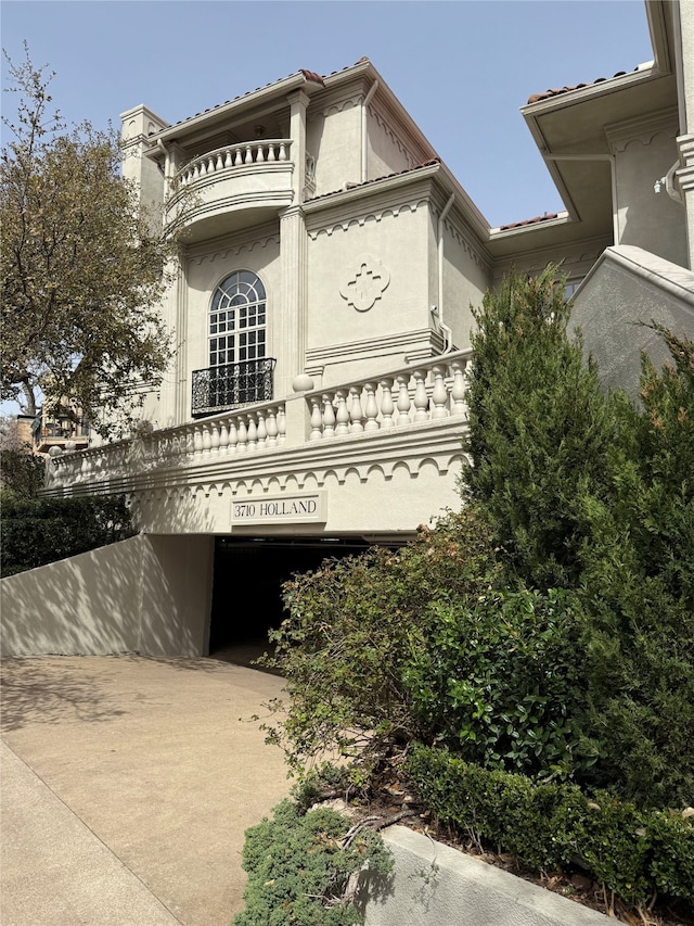 view of side of home featuring concrete driveway, a balcony, and stucco siding