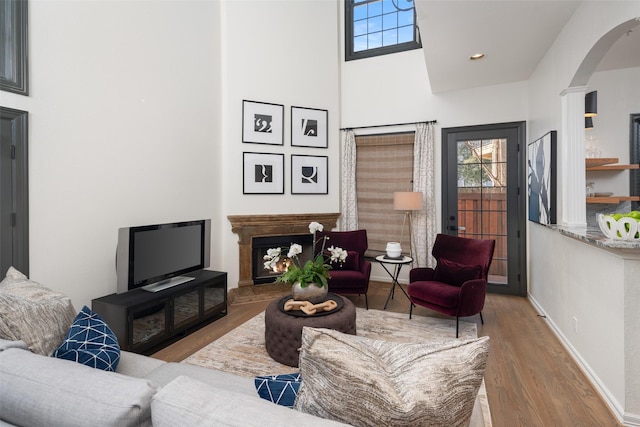 living room featuring arched walkways, a high ceiling, wood finished floors, a warm lit fireplace, and baseboards