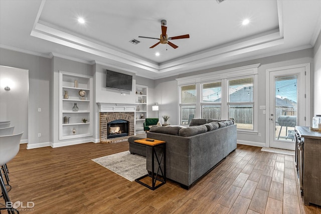 living area with a raised ceiling, visible vents, a brick fireplace, wood finished floors, and baseboards