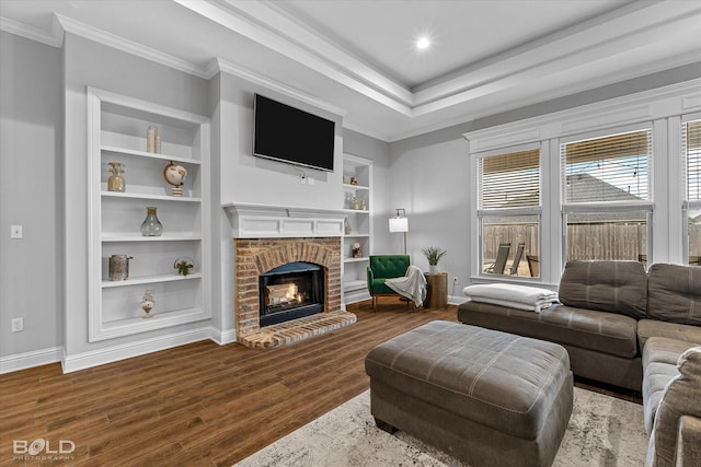 living room featuring built in shelves, a fireplace, wood finished floors, baseboards, and ornamental molding