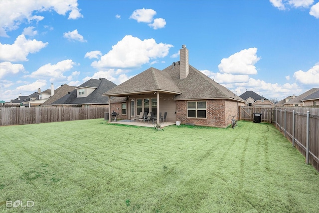 back of property with a fenced backyard, a chimney, a lawn, and brick siding