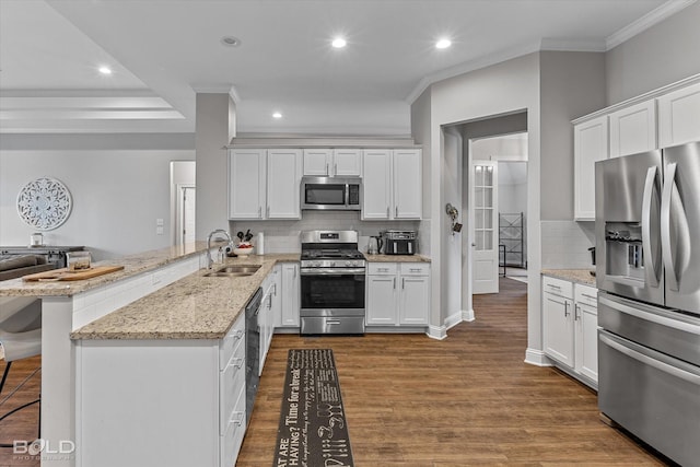 kitchen with a breakfast bar area, stainless steel appliances, white cabinetry, a sink, and a peninsula