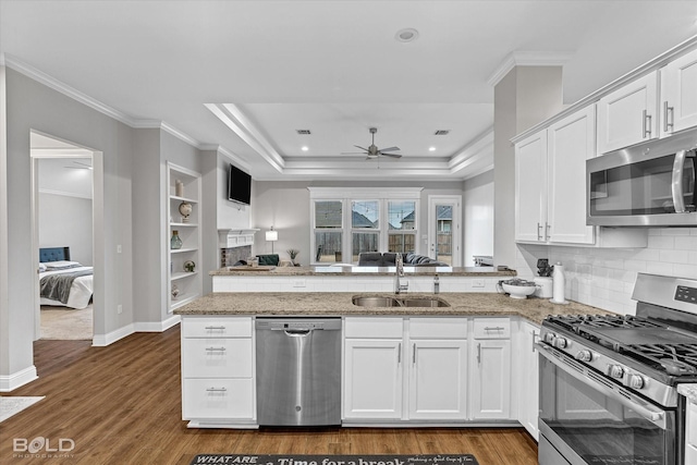 kitchen featuring open floor plan, a peninsula, stainless steel appliances, white cabinetry, and a sink