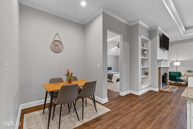 dining space featuring built in features, crown molding, dark wood-type flooring, a brick fireplace, and baseboards