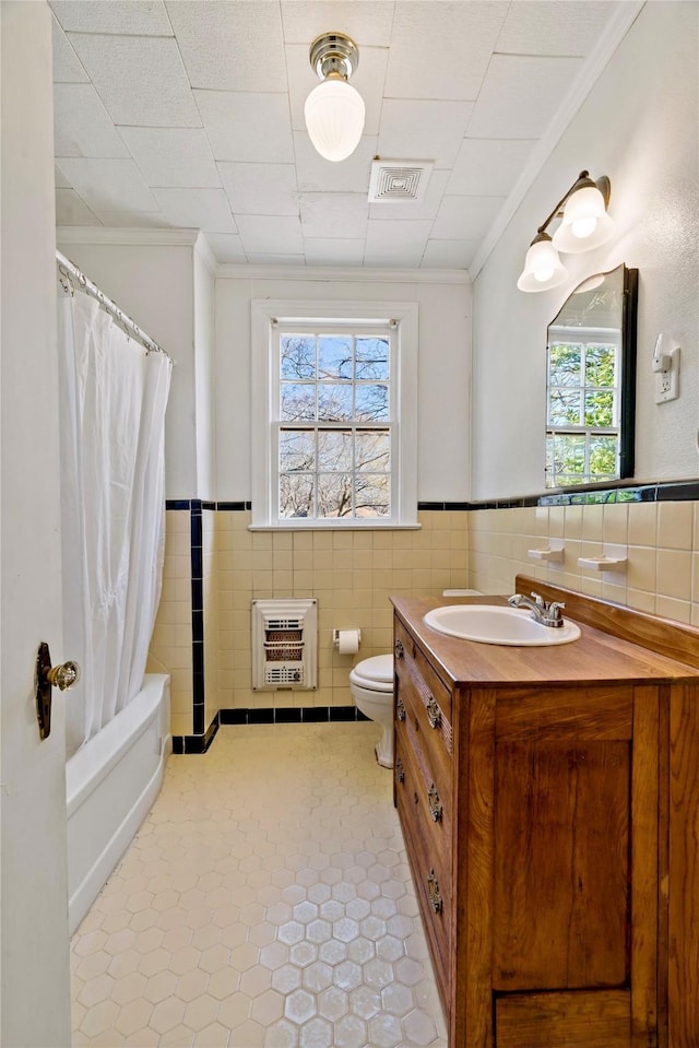 bathroom with a wainscoted wall, tile walls, heating unit, visible vents, and vanity