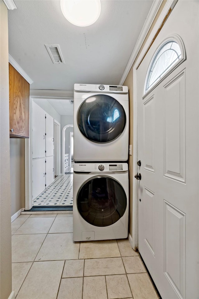 clothes washing area featuring light tile patterned floors, laundry area, visible vents, arched walkways, and stacked washing maching and dryer