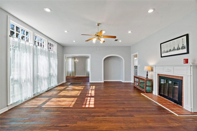 unfurnished living room featuring arched walkways, dark wood-style flooring, a tiled fireplace, and recessed lighting