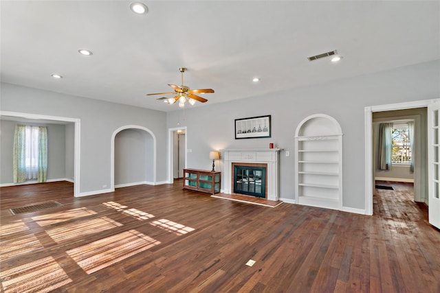 unfurnished living room featuring arched walkways, visible vents, built in features, dark wood-style floors, and a glass covered fireplace