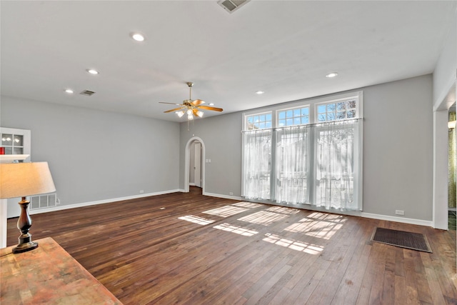 unfurnished living room featuring dark wood-style floors, visible vents, and arched walkways