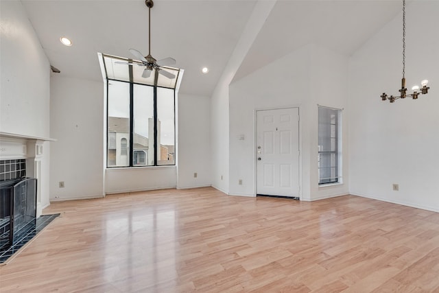 unfurnished living room with light wood-type flooring, high vaulted ceiling, ceiling fan with notable chandelier, and a tile fireplace