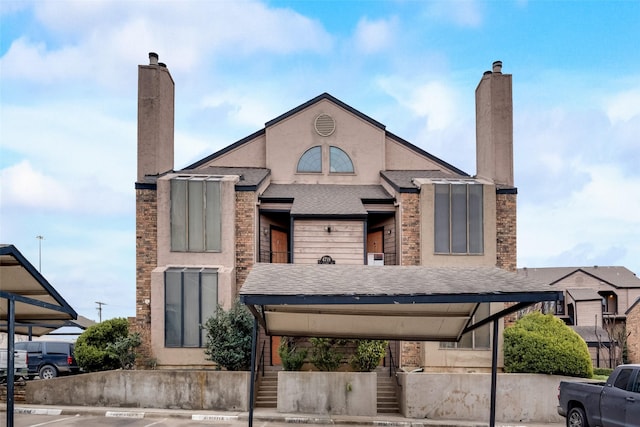 view of front of home featuring stairs, roof with shingles, stucco siding, a chimney, and covered and uncovered parking