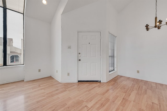 interior space featuring high vaulted ceiling, light wood-type flooring, baseboards, and an inviting chandelier