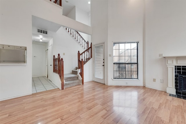 unfurnished living room featuring light wood-type flooring, visible vents, and a tiled fireplace