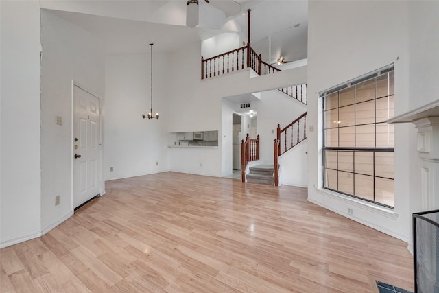 unfurnished living room with a notable chandelier, a high ceiling, visible vents, stairs, and light wood-type flooring