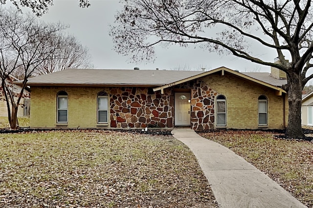 ranch-style house featuring stone siding, brick siding, and a front lawn