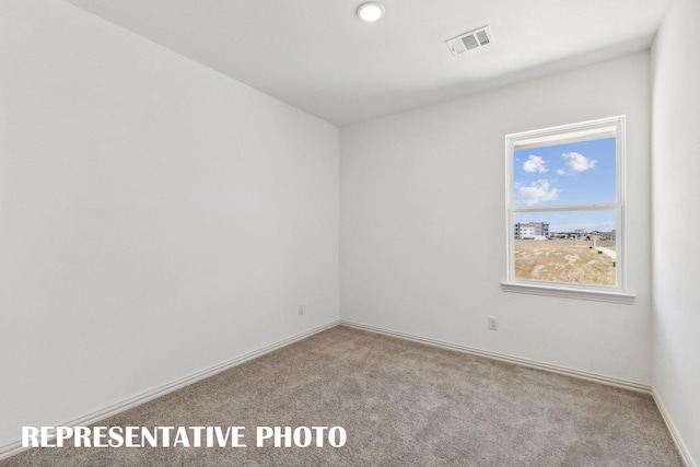 spare room featuring light colored carpet, visible vents, and baseboards