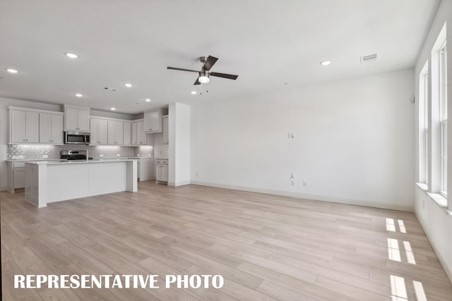 kitchen with a kitchen island with sink, stainless steel appliances, open floor plan, light countertops, and tasteful backsplash