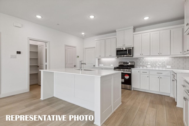 kitchen featuring a kitchen island with sink, white cabinetry, stainless steel appliances, and light countertops