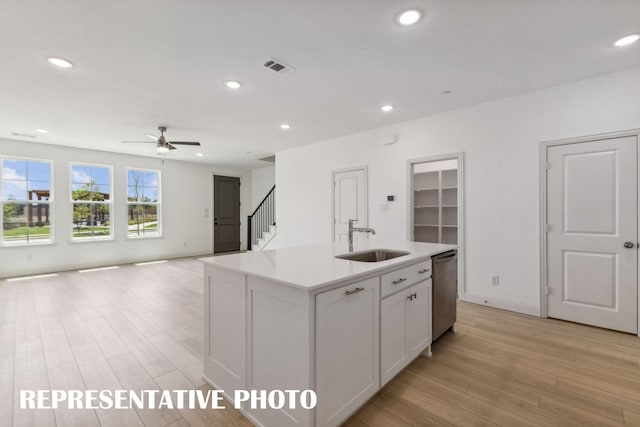 kitchen featuring white cabinets, an island with sink, open floor plan, a sink, and stainless steel dishwasher