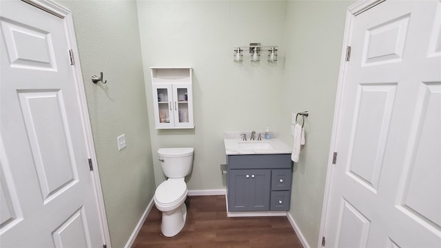 half bath with toilet, baseboards, wood finished floors, and vanity